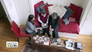 Jessica Gomez is sitting next to two women looking at a scrapbook while sitting on red chairs