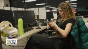student sits in front a desktop computer while looking at her phone