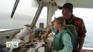 a male fisherman and his son look out boat window